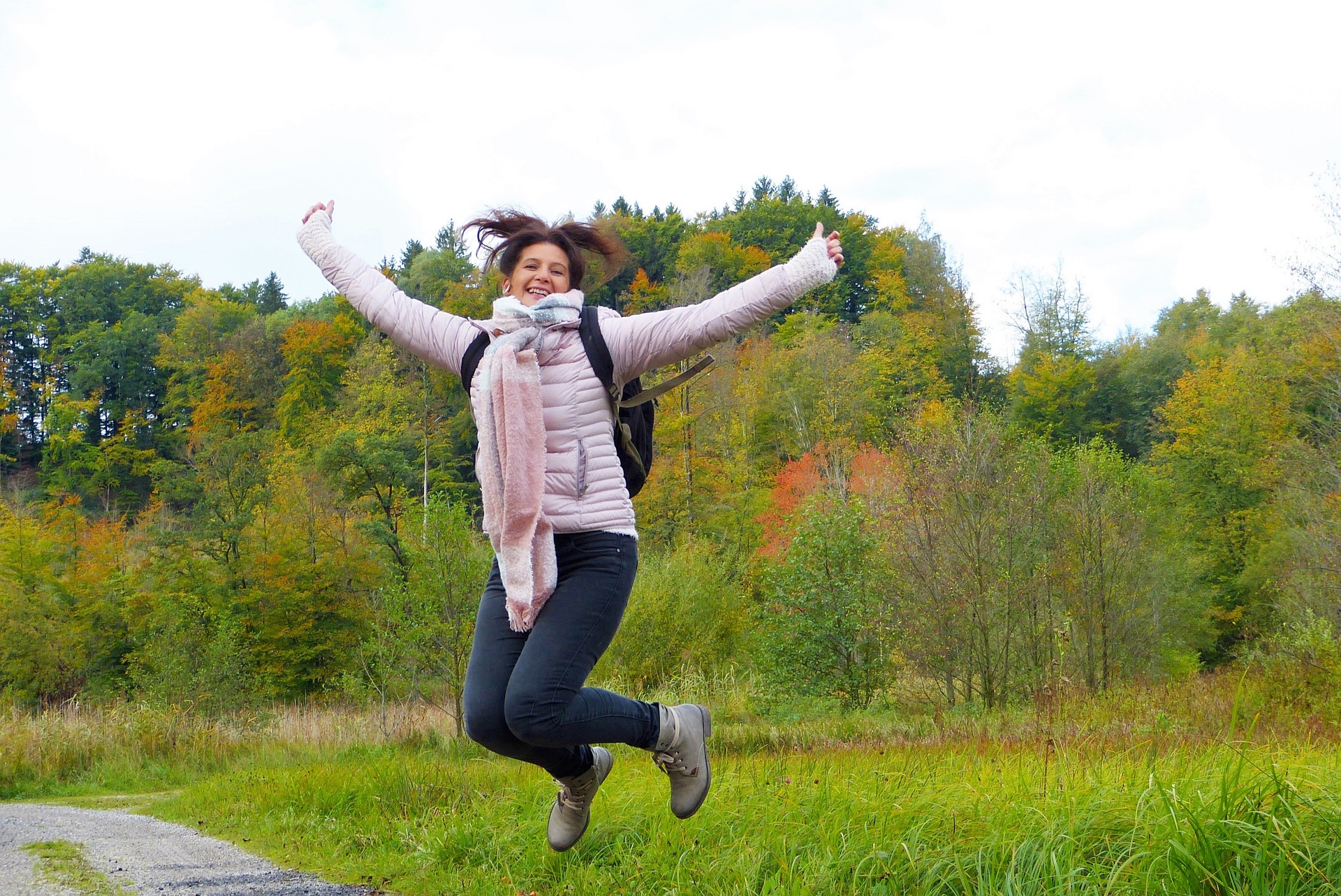 Woman wearing hiking gear jumping on forested path