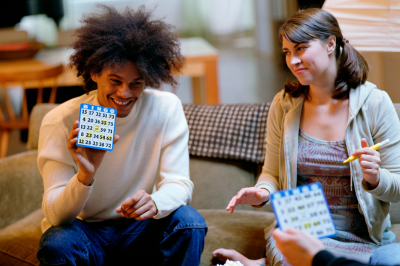 Bingo night with friends: Young man holding up winning bingo card sitting next to young woman on a living room couch