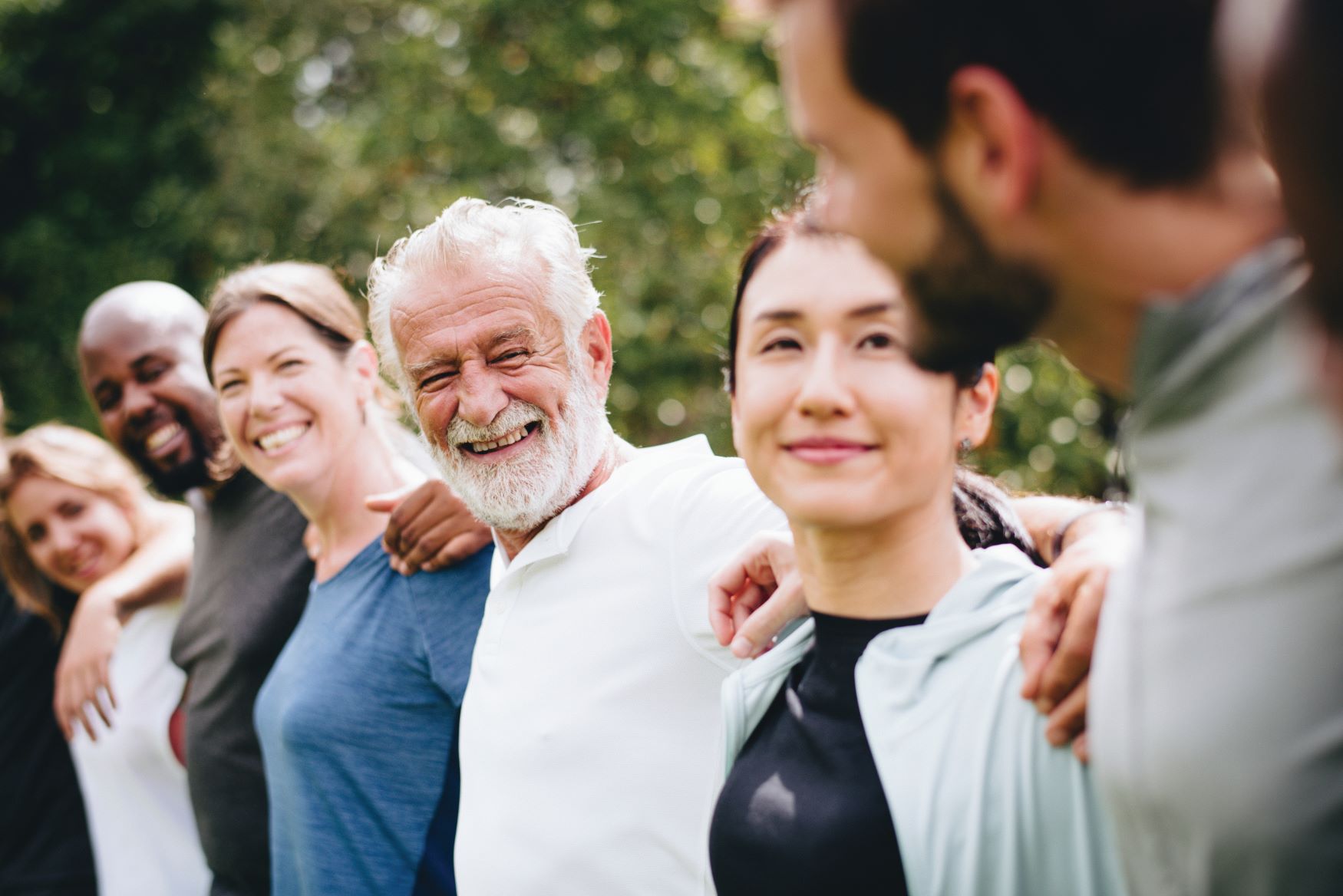 Line of smiling older people in workout clothes standing with arms around each other's shoulders