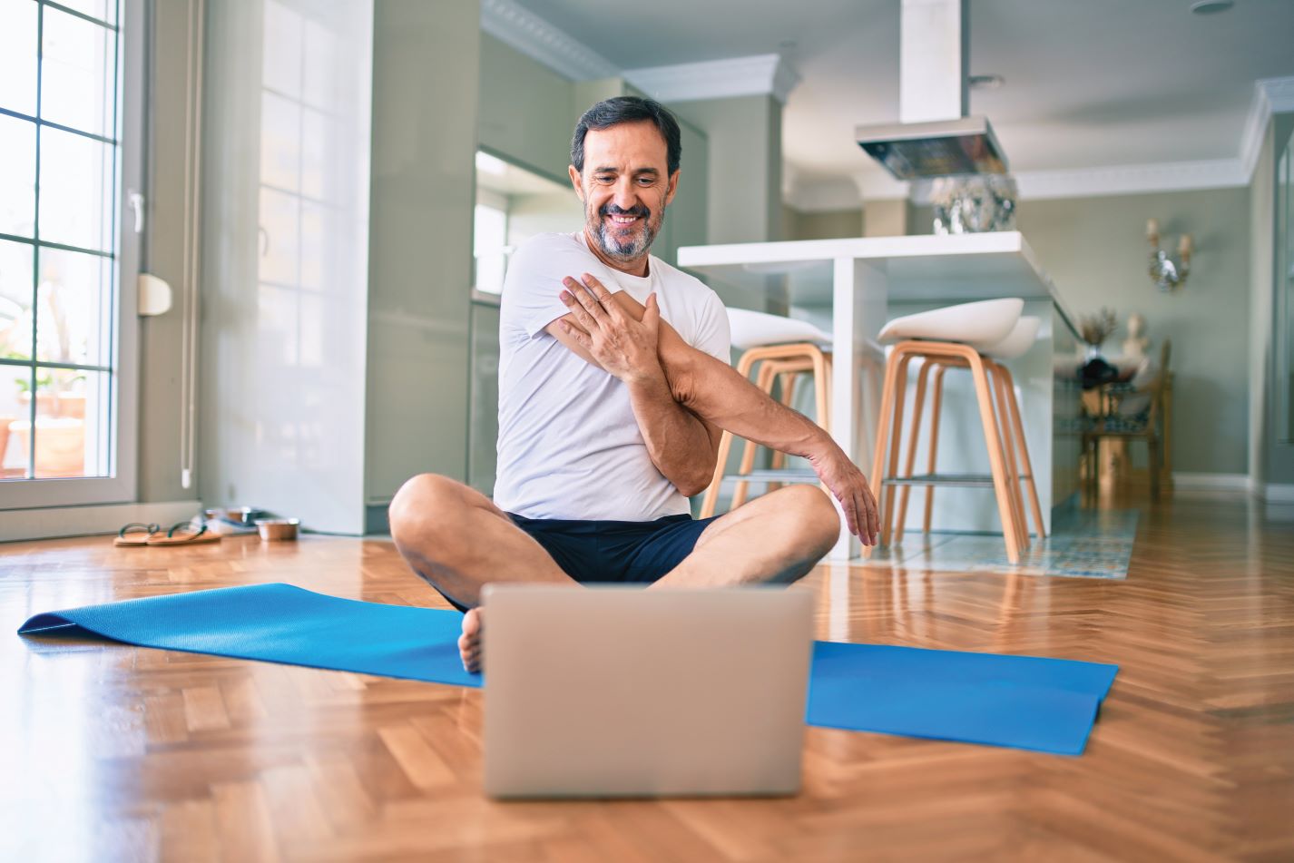 Middle-aged man sitting on yoga mat at home stretching his tricep