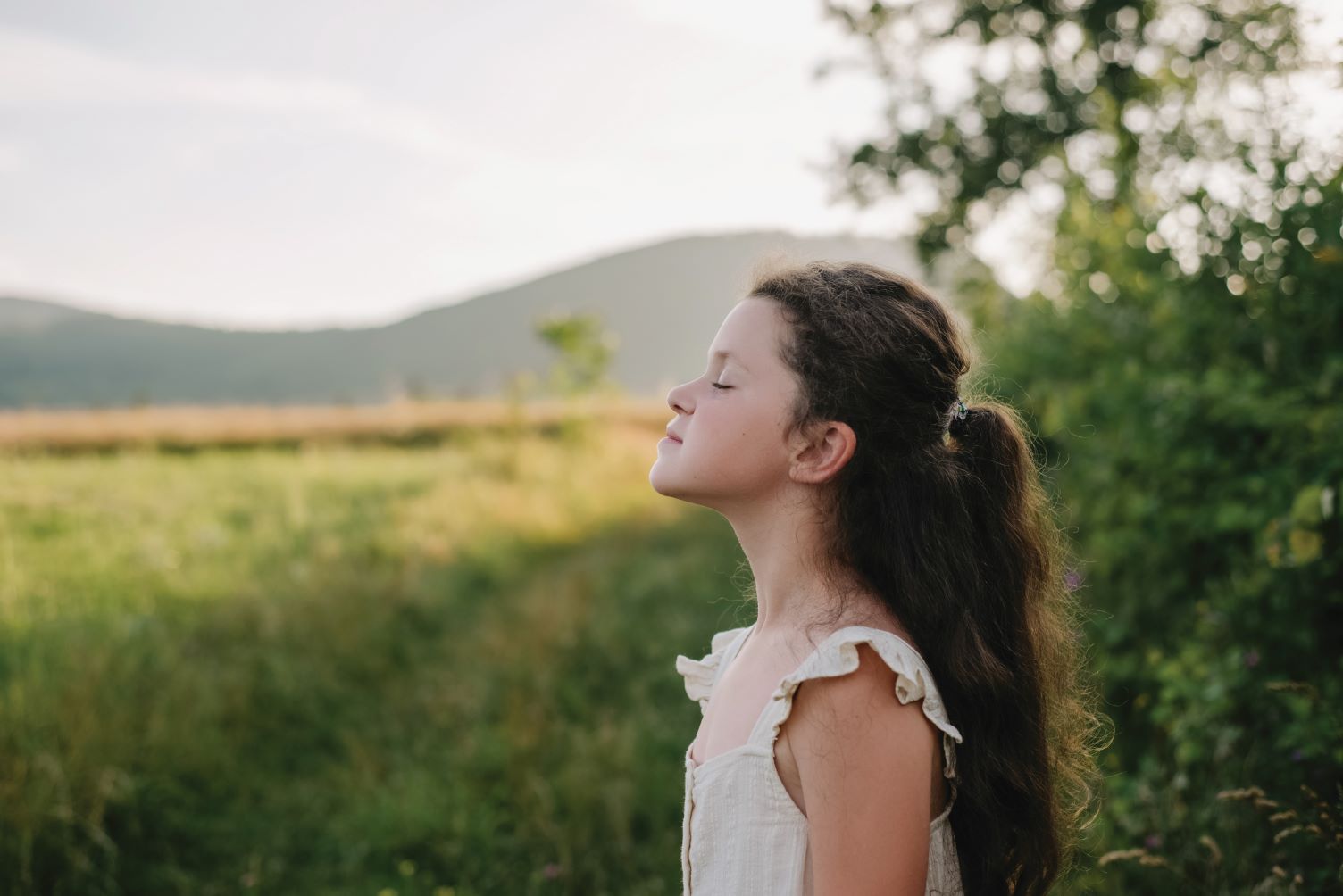 Young girl standing on edge of green field taking a deep breath in